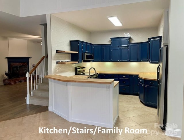 kitchen featuring blue cabinets, light tile patterned floors, a fireplace, kitchen peninsula, and stainless steel appliances