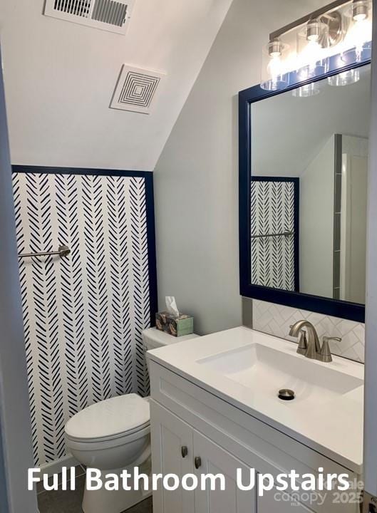 bathroom featuring vanity, toilet, and lofted ceiling