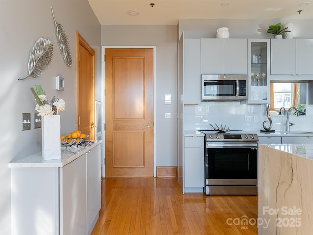 kitchen featuring backsplash, white cabinets, sink, light stone countertops, and appliances with stainless steel finishes