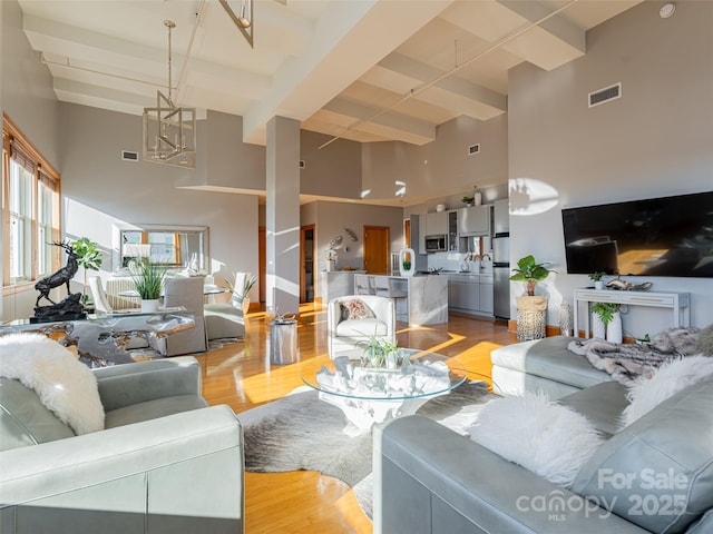 living room with beam ceiling, light hardwood / wood-style floors, and a high ceiling