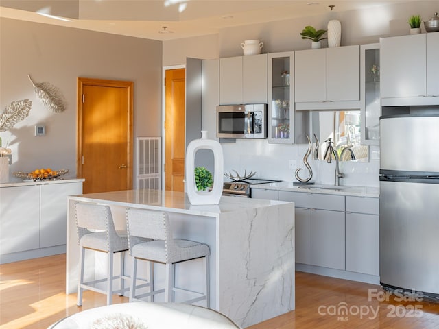 kitchen featuring sink, light wood-type flooring, appliances with stainless steel finishes, tasteful backsplash, and a kitchen island