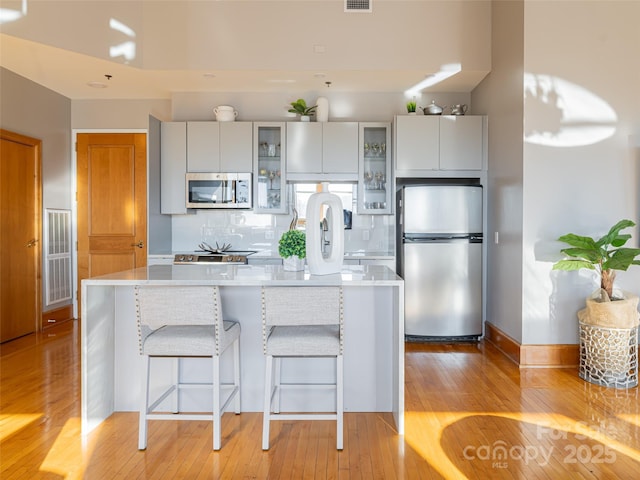 kitchen featuring a center island, stainless steel appliances, tasteful backsplash, light hardwood / wood-style flooring, and a kitchen bar