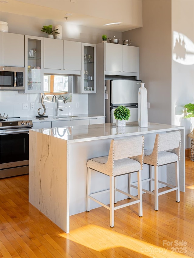 kitchen featuring sink, stainless steel appliances, a kitchen breakfast bar, backsplash, and light wood-type flooring