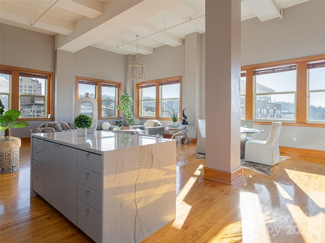 kitchen with beamed ceiling, pendant lighting, light wood-type flooring, and light stone counters