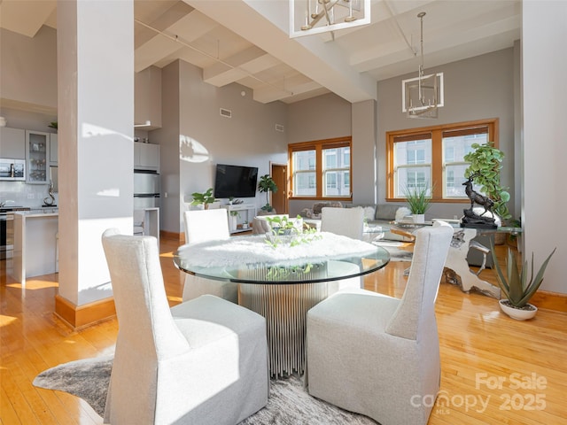 dining area featuring beam ceiling, a high ceiling, and light hardwood / wood-style flooring