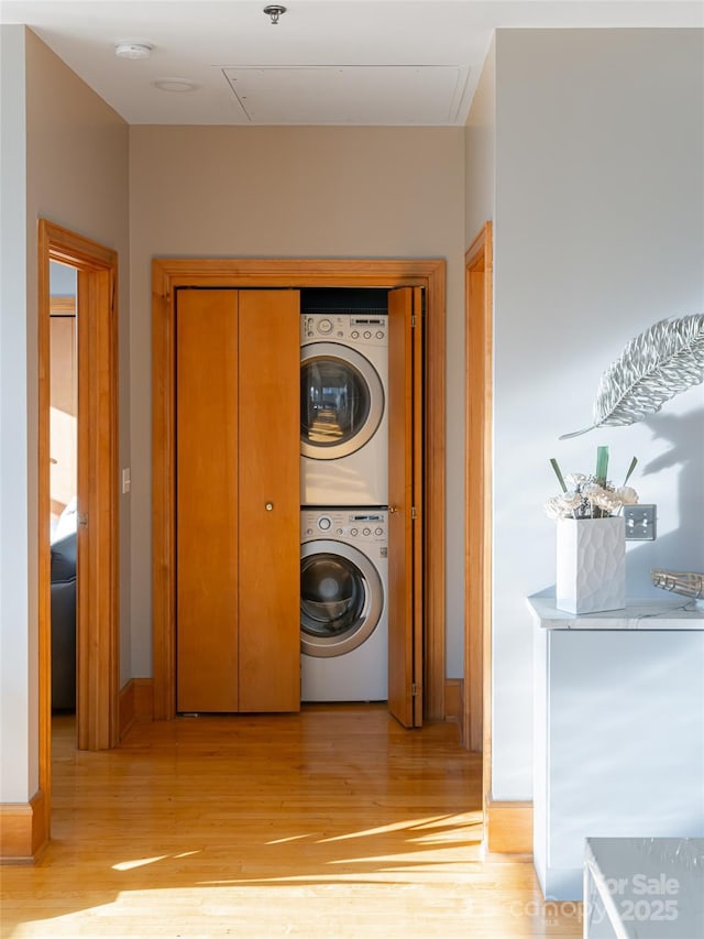 laundry room with light wood-type flooring and stacked washer / dryer