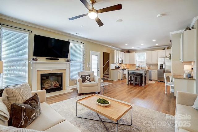 living room with light hardwood / wood-style flooring, ceiling fan, and crown molding