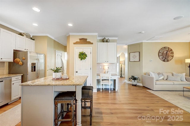 kitchen with stainless steel appliances, a kitchen island, a breakfast bar, white cabinets, and light wood-type flooring