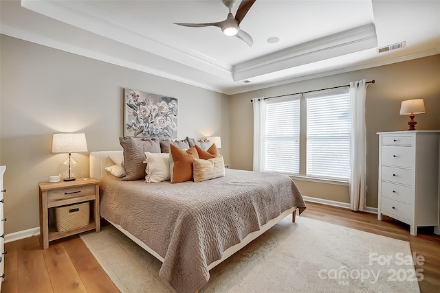 bedroom with wood-type flooring, a tray ceiling, ceiling fan, and ornamental molding