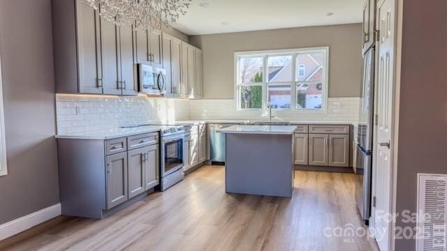 kitchen featuring appliances with stainless steel finishes, sink, an inviting chandelier, light hardwood / wood-style flooring, and a center island