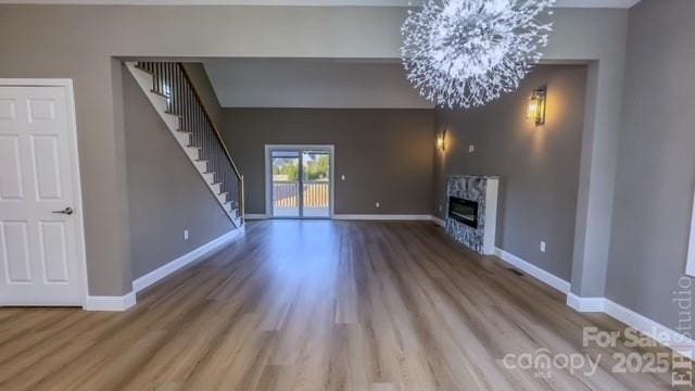 unfurnished living room with a premium fireplace, wood-type flooring, and a notable chandelier