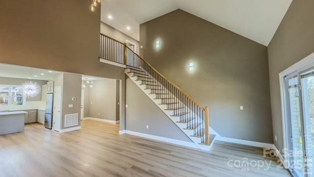 unfurnished living room with light hardwood / wood-style floors, high vaulted ceiling, and an inviting chandelier