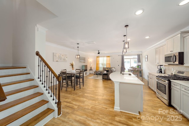 kitchen with ceiling fan, sink, decorative light fixtures, a kitchen island with sink, and appliances with stainless steel finishes