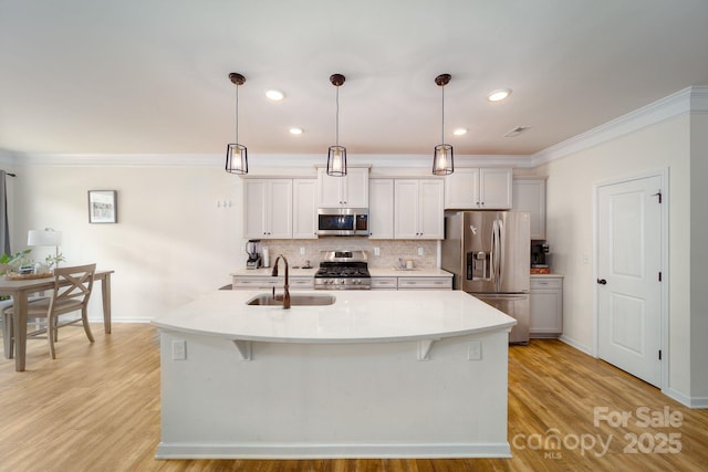 kitchen featuring a kitchen island with sink, sink, stainless steel appliances, and hanging light fixtures