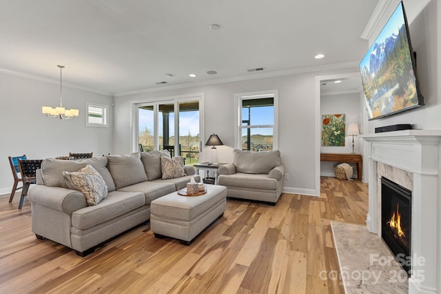 living room with a premium fireplace, crown molding, light wood-type flooring, and an inviting chandelier