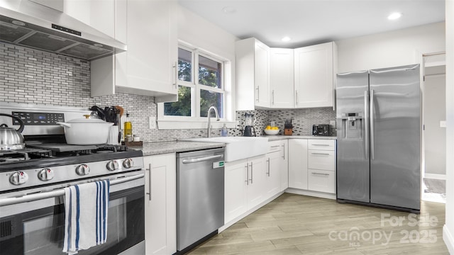 kitchen with appliances with stainless steel finishes, tasteful backsplash, wall chimney exhaust hood, sink, and white cabinetry