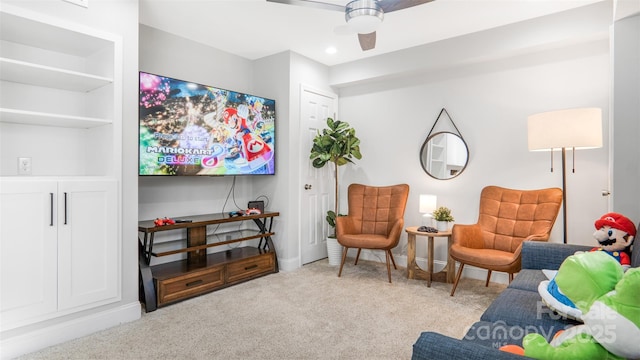 sitting room featuring built in shelves, ceiling fan, and light carpet