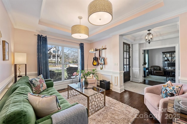 living room with a tray ceiling, crown molding, dark wood-type flooring, and a notable chandelier