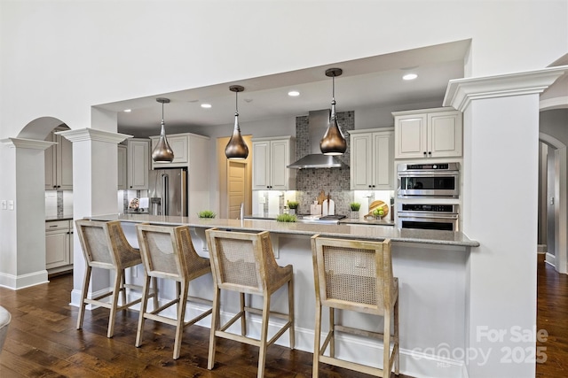 kitchen with a kitchen bar, decorative light fixtures, stainless steel appliances, and wall chimney range hood