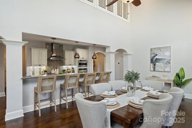 dining room with a high ceiling, dark hardwood / wood-style floors, ceiling fan, and decorative columns