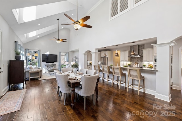 dining room with a high ceiling, dark hardwood / wood-style flooring, a skylight, and ceiling fan