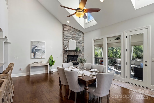 dining area with ceiling fan, a stone fireplace, lofted ceiling with skylight, and a wealth of natural light