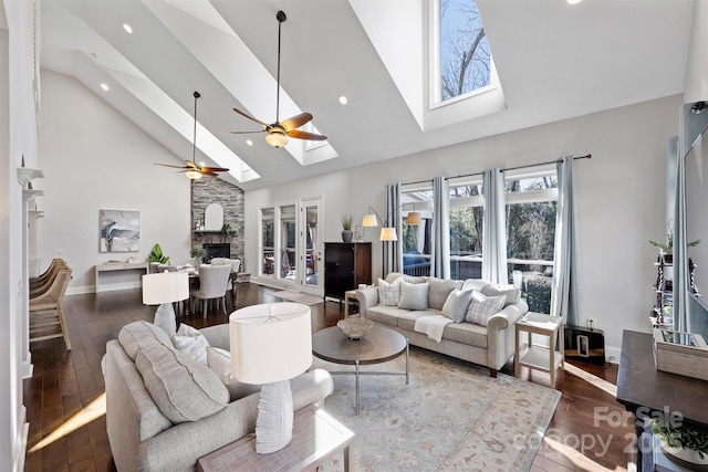 living room with high vaulted ceiling, a skylight, a stone fireplace, and ceiling fan