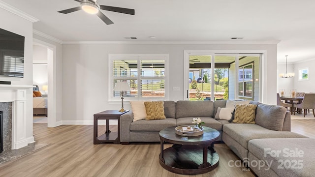 living room featuring a healthy amount of sunlight, ornamental molding, ceiling fan with notable chandelier, and light wood-type flooring