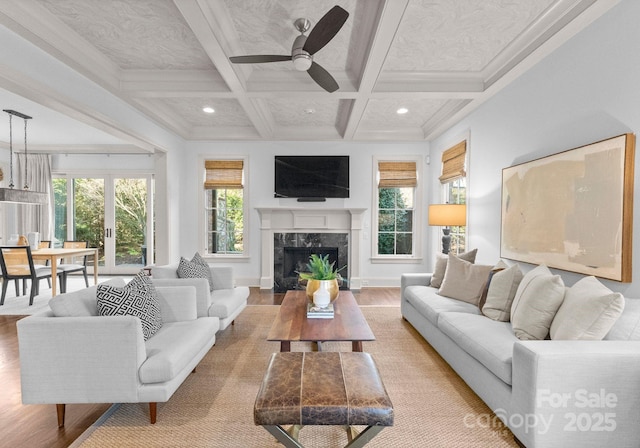 living room with beamed ceiling, coffered ceiling, ceiling fan, a high end fireplace, and light hardwood / wood-style floors