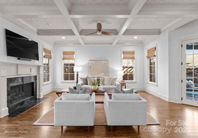 living room with beamed ceiling, wood-type flooring, coffered ceiling, ceiling fan, and a premium fireplace