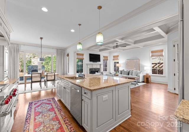 kitchen featuring sink, hanging light fixtures, a center island with sink, appliances with stainless steel finishes, and light stone countertops