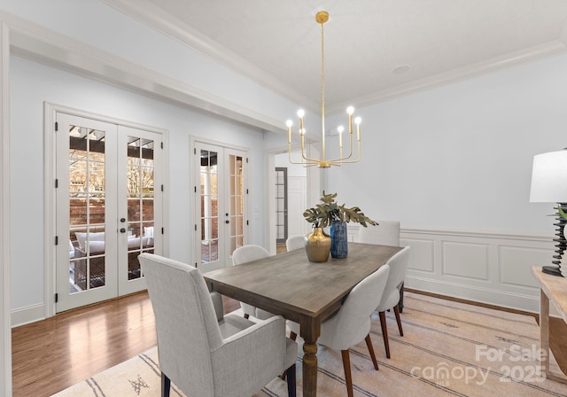 dining space with french doors, crown molding, a chandelier, and light wood-type flooring