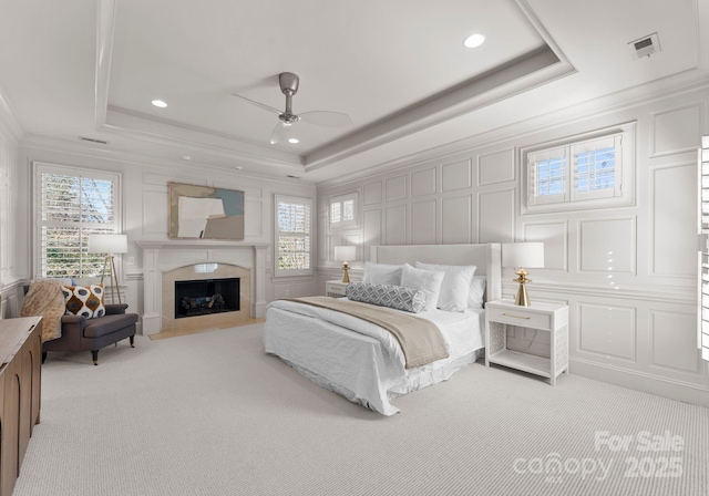 carpeted bedroom featuring crown molding, a tray ceiling, and a fireplace