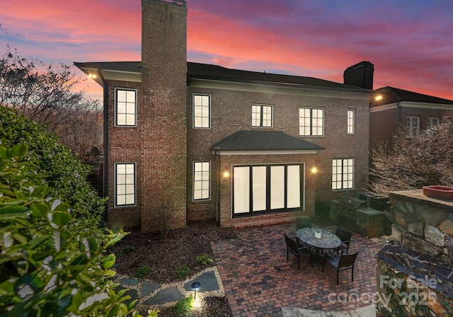 back house at dusk featuring a patio area and an outdoor kitchen