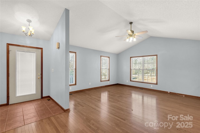 foyer entrance with ceiling fan with notable chandelier, hardwood / wood-style flooring, and vaulted ceiling