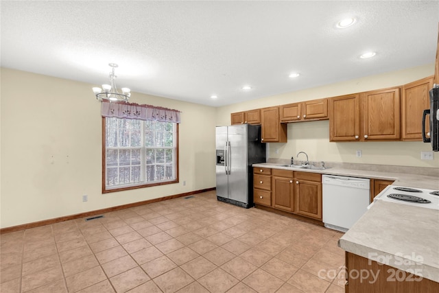 kitchen featuring stainless steel fridge, white dishwasher, sink, decorative light fixtures, and an inviting chandelier