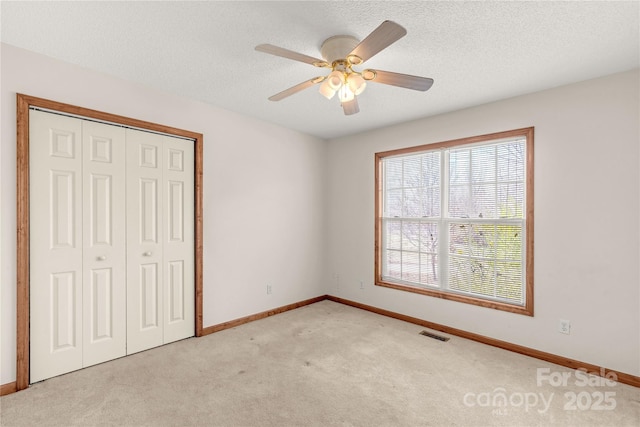 unfurnished bedroom featuring ceiling fan, light colored carpet, a textured ceiling, and a closet