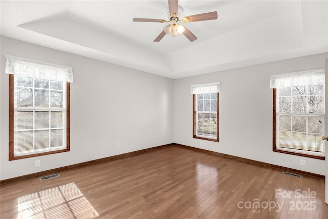 empty room with hardwood / wood-style flooring, ceiling fan, a healthy amount of sunlight, and a tray ceiling