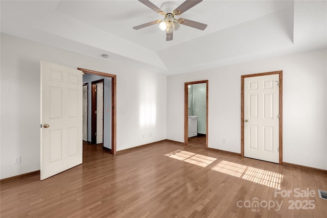 unfurnished bedroom featuring hardwood / wood-style floors, ensuite bathroom, a raised ceiling, and ceiling fan