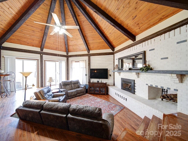 living room with light wood-type flooring, a brick fireplace, ceiling fan, wooden ceiling, and beamed ceiling