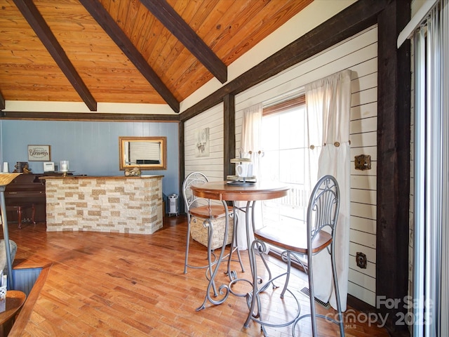 dining space featuring lofted ceiling with beams, wood walls, and wood ceiling