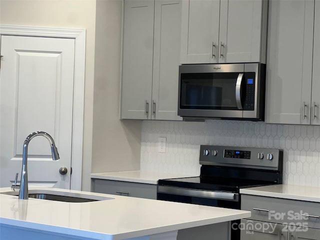 kitchen with stainless steel appliances, an island with sink, sink, and gray cabinets