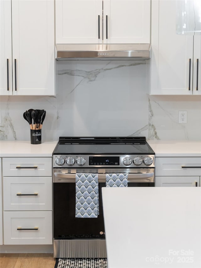 kitchen featuring decorative backsplash, stainless steel range, and white cabinets