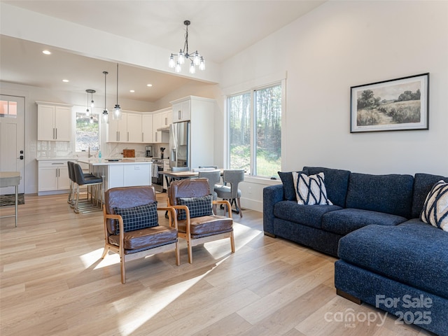 living room featuring light wood-type flooring, lofted ceiling, sink, and a chandelier