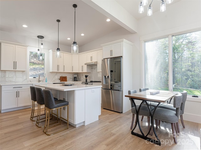 kitchen with backsplash, a kitchen island, pendant lighting, stainless steel fridge with ice dispenser, and white cabinetry