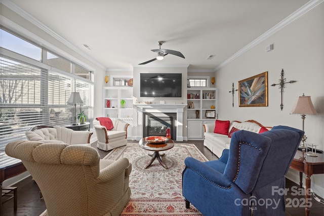 living room featuring built in shelves, ceiling fan, crown molding, and hardwood / wood-style floors