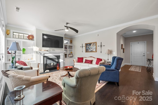 living room with built in shelves, ceiling fan, dark hardwood / wood-style floors, and ornamental molding