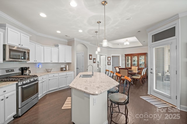 kitchen featuring a kitchen island with sink, sink, decorative light fixtures, white cabinetry, and stainless steel appliances