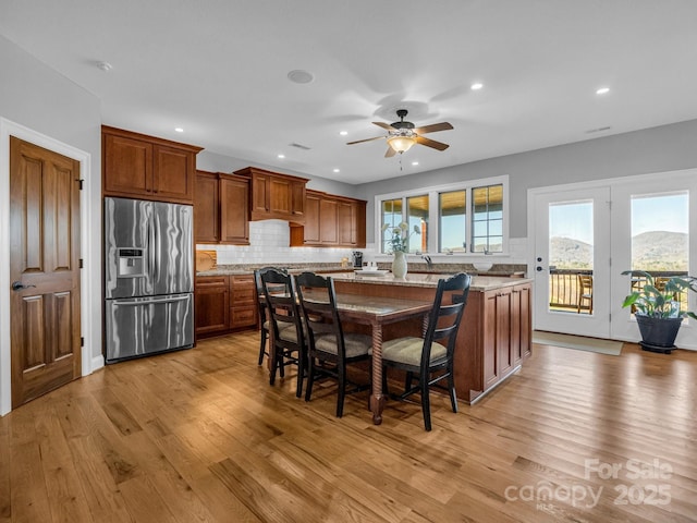 kitchen with light stone counters, a center island, stainless steel fridge with ice dispenser, light hardwood / wood-style floors, and a breakfast bar area