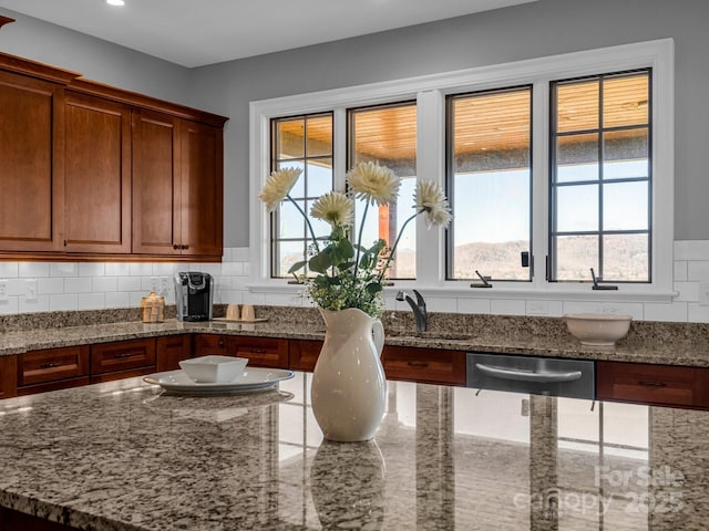 kitchen with stainless steel dishwasher, decorative backsplash, sink, and light stone counters